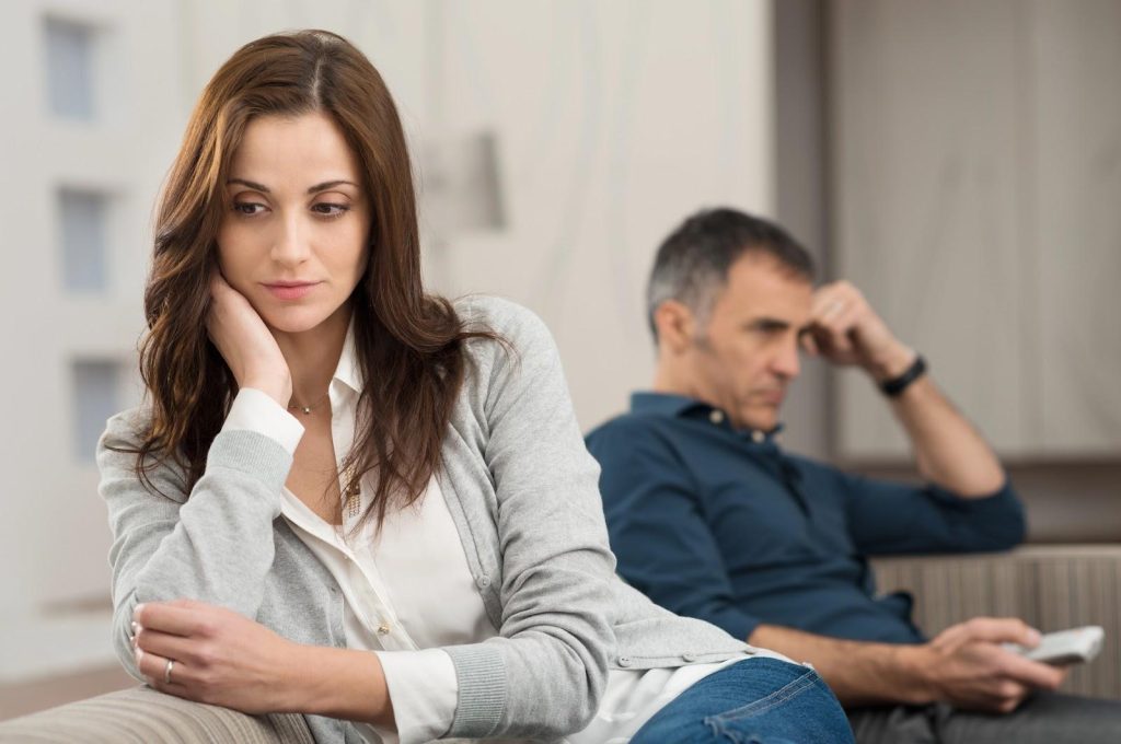 A couple sitting on opposite ends of a couch and not looking at one another.