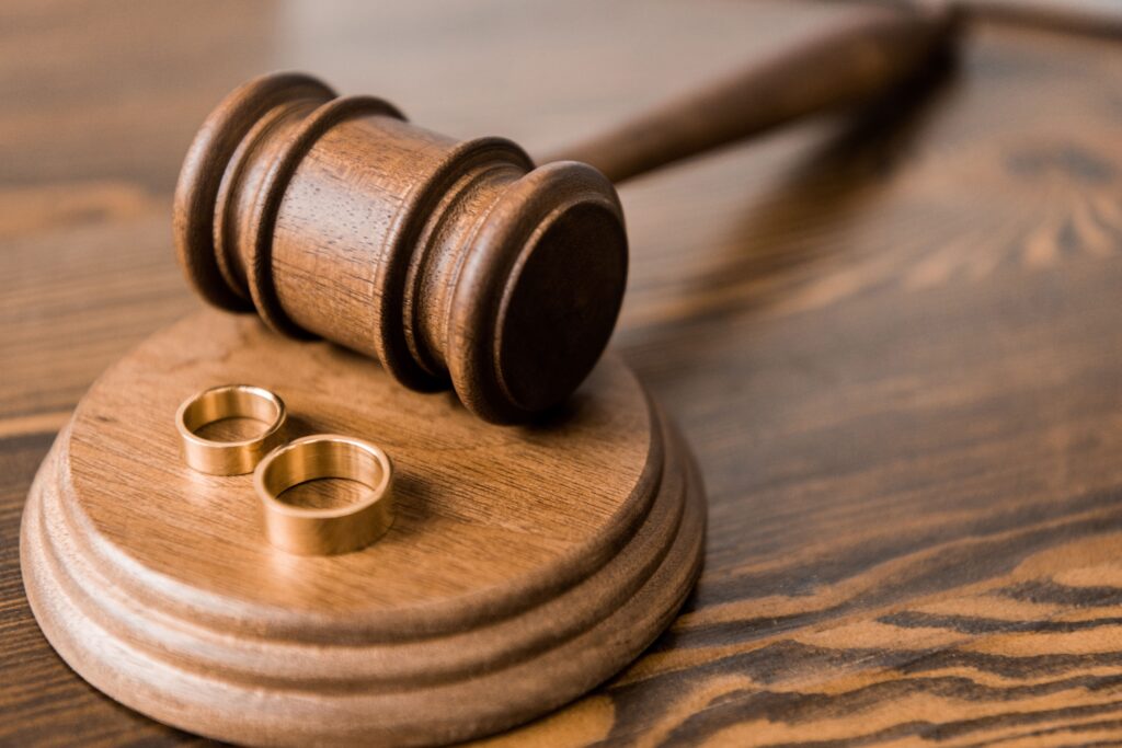 A close-up of a wooden gavel resting on its sound block with two gold wedding bands placed beside it on a wood-grain surface, symbolizing a divorce legal proceeding in Phoenix, Arizona.